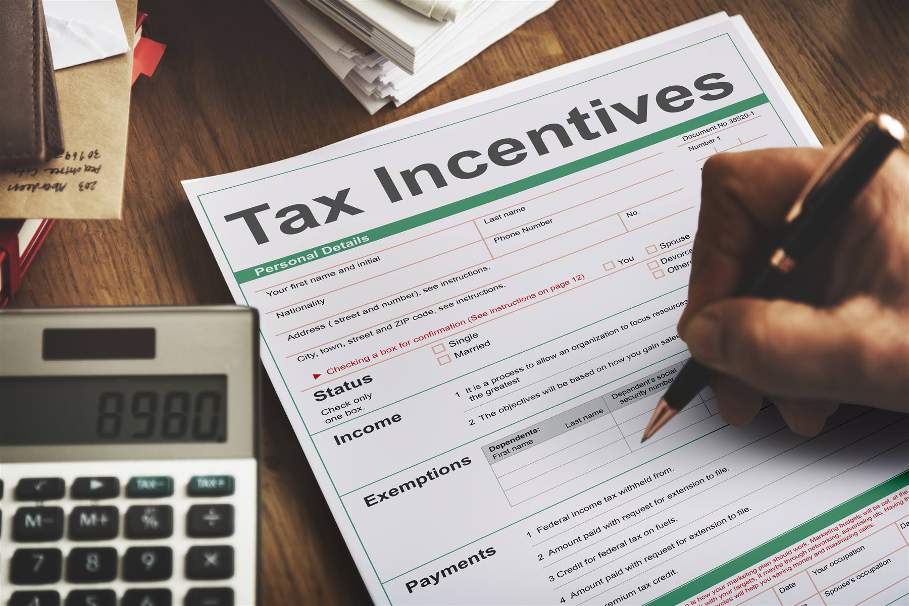 A paper tax form being filled in by hand next to a calculator